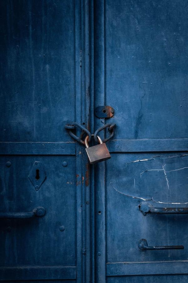 A padlock and chain holding a weathered blue metal double door shut